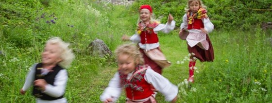 Glada barn som springer på en äng i sina daladräkter.
