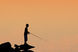 Siluett av barn som fiskar i solnedgång.