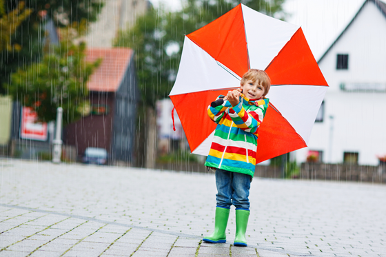 Ett barn i färgglada regnkläder håller ett stort paraply