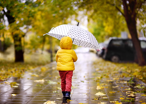Ett barn i färgglada kläder och paraply går längs en trottoar