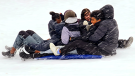 En grupp glada ungdomar åker skrana i snöfall.