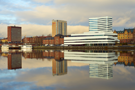 Umeå stads byggnader vid kajen speglas i älvsvatten.