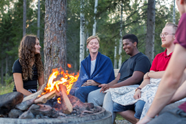 Unga personer sitter vid en eld utomhus