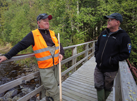 Två män i samtal på en träbro i skogen