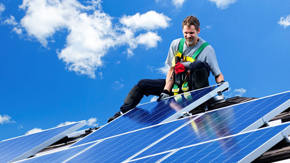 Man som installerar solceller på ett tak med blå himmel i bakgrunden.
