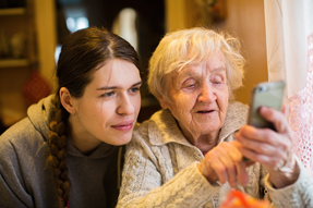 Bild på yngre kvinna som hjälper äldre kvinna med en smart telefon.