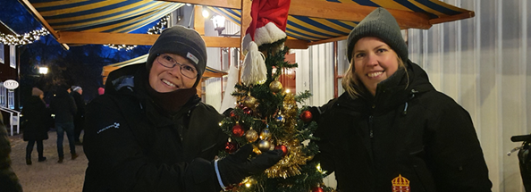Åsa Lindin och Josefine Eklund poserar på var sin sida om julgran på julmarknad