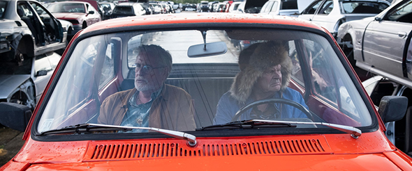 Foto från filmen, två män sitter i en röd bil.