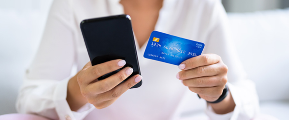 Foto på kvinna som håller i en mobil och ett bankkort.