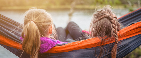 Två flickor i hängmatta ser ut över sjö, foto.
