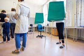 Syntolkning av bild: Valbås i en vallokal med väljare som röstar.