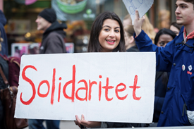 Syntolkning av bild: En tjej håller i ett plakat med texten Solidaritet. Hon befinner sig i ett demonstrationståg. Foto från partistyrelsens bildbank.
